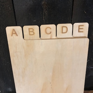 May include: A wooden index card holder with five tabs labelled A, B, C, D, and E. The holder is made of light-coloured wood and has a natural finish.
