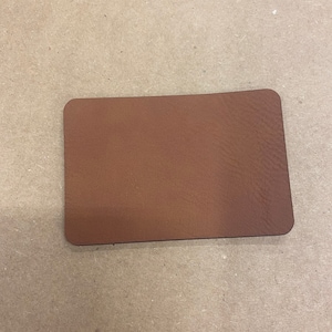 May include: A close-up of a brown leather patch. The patch is smooth and has a slightly textured surface.
