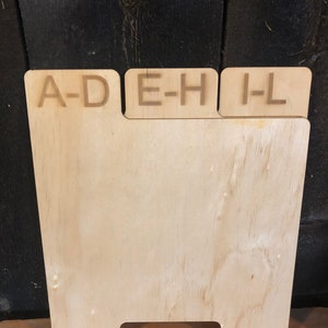 Puede incluir: Un divisor de madera con tres secciones etiquetadas "A-D", "E-H" e "I-L".