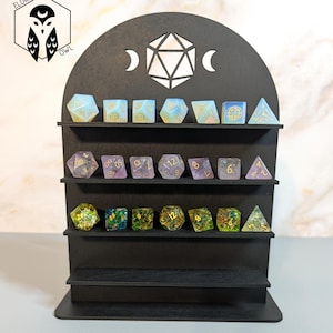 Könnte beinhalten: Ein schwarzer Würfel-Präsentationsständer aus Holz mit drei Regalen, der eine Sammlung farbenfroher polyedrischer Würfel enthält. Der Ständer hat eine dekorative Oberseite mit einem geometrischen Design und Halbmonden. Der Text "SVG - DIGITAL FILE ONLY" steht unten.