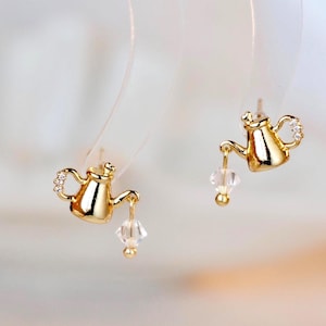 Puede incluir: Una taza de cerámica blanca con un asa negra y el texto "But First, Coffee" en negrita negra. La taza se encuentra sobre un fondo borroso, resaltando su diseño simple.