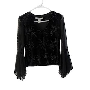 May include: A black long-sleeve top featuring a V-neckline and sheer mesh bell sleeves. The bodice is made of a velvet-like fabric with a subtle, tonal floral pattern. A white clothing tag at the neckline displays the text J.R. NITE PETITES.