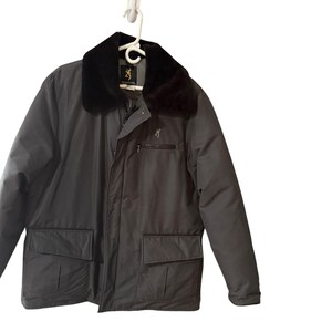 May include: A gray Browning jacket with a black faux fur collar. The jacket has a zipper closure, two front pockets, and a small chest pocket. The Browning logo is visible on the chest. The jacket is hanging on a white hanger.
