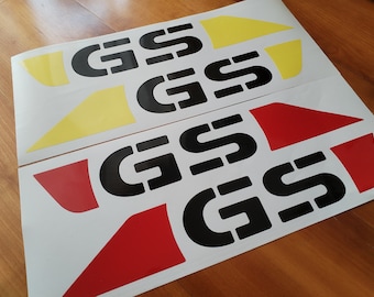 Könnte beinhalten: Vier weiße Blätter mit schwarzer Beschriftung "GS" und gelben und roten Akzenten.