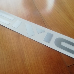 Peut inclure: Un autocollant d'emblème de voiture "CIVIC" argenté sur fond blanc.