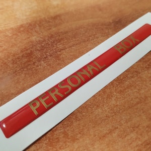 May include: A red label with the words "PERSONAL BOX" in gold lettering.