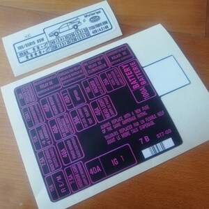 Puede incluir: Pegatina de diagrama de caja de fusibles negra y rosa con el texto "100A Battery" y "Siempre reemplace con un fusible nuevo de la misma intensidad.  Toujours remplacer par un fusible neuf avant le meme taux d'aperage." La pegatina también incluye un código de barras y el texto "7B ST7-GO".