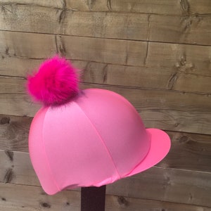Può includere: Cappello da equitazione rosa con un pompon in pelliccia sintetica rosa in cima.