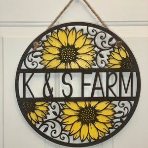 May include: A round wooden sign with a brown background and yellow sunflowers. The sign says "K & S FARM" in black letters.