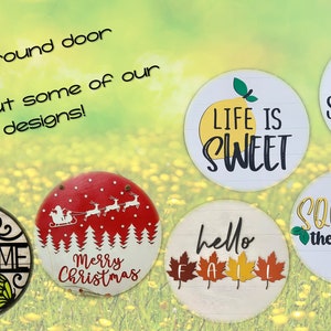 May include: A collection of round wooden signs with various designs and sayings. The signs feature phrases like "Life is Sweet", "Hello Summer", "Squeeze the Day", "Welcome", "Hello Fall", and "Merry Christmas".
