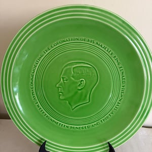 May include: A green ceramic plate with a portrait of a man and text around the rim. The text reads "Commemorating the Coronation of His Majesty King Edward VIII. 1937." The plate is displayed on a black stand.
