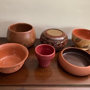Op de afbeelding: Zes terracotta potten in verschillende maten en vormen. De potten zijn allemaal roodbruin van kleur en hebben een geglazuurde afwerking. Sommige potten hebben decoratieve patronen.
