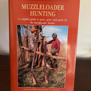 May include: A hardcover book titled MUZZLELOADER HUNTING from the NRA Hunter Skills Series. The orange cover features a photograph of two hunters in a wooded area with two muzzleloader rifles standing upright in the foreground.