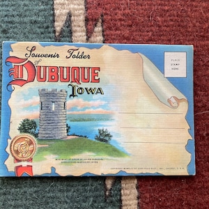 Puede incluir: Una postal vintage con un dibujo de un monumento de piedra con vistas a un río. La postal dice "Souvenir Folder of DUBUQUE IOWA" y "Monument at Grave of Julien Dubuque, Overlooking Mississippi River".