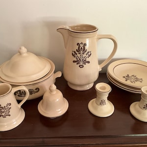 May include: A set of brown and cream colored ceramic kitchenware with a floral design. The set includes a pitcher, a casserole dish with lid, a creamer, a sugar bowl, and two candle holders.