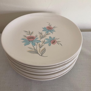 Può includere: Un set di dieci piatti da portata in ceramica bianca con un motivo floreale in tonalità di blu, rosa e verde.