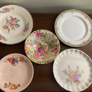 May include: Five floral patterned ceramic plates in various sizes and designs. The plates feature pink, yellow, and green floral patterns.