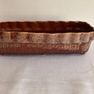 May include: A brown and white ceramic planter with a wavy rim and a textured surface.