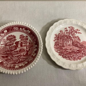 May include: Two white ceramic plates with red and white floral designs. The plates feature a red and white floral pattern with a scene of a bridge and a castle.