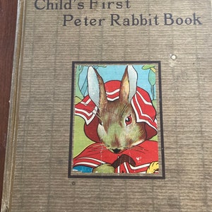 May include: A vintage book titled "Child's First Peter Rabbit Book" with a brown cover and a picture of Peter Rabbit wearing a red and white hooded jacket.