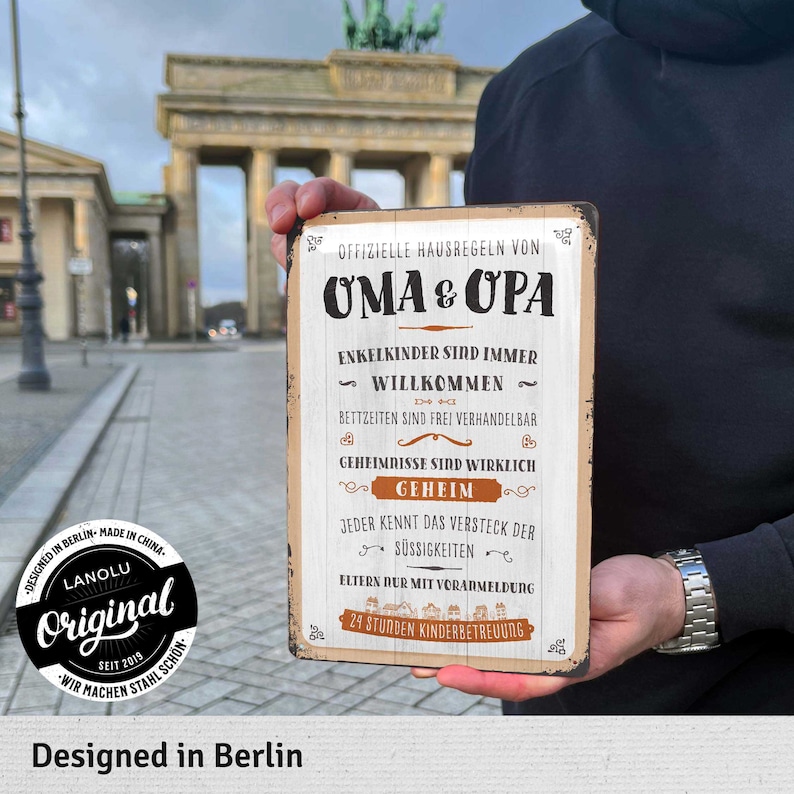 Pu&ograve; includere: Un cartello metallico rettangolare con testo tedesco, tra cui "OMA & OPA" e "OFFIZIELLE HAUSREGELN". Il cartello ha un aspetto vintage e presenta regole familiari. Lo sfondo mostra la Porta di Brandeburgo a Berlino.