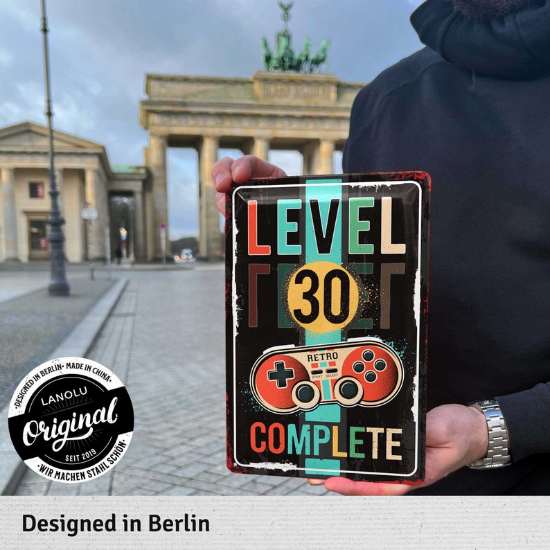 May include: A rectangular metal sign with the words "LEVEL 30 COMPLETE" and a retro video game controller graphic. The sign is black with red, green, and teal accents. The sign also says "Designed in Berlin".