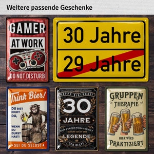 May include: Collection of vintage-style metal signs with various designs. One sign reads "GAMER AT WORK" with a retro game controller. Another says "30 Jahre" and "29 Jahre". Other signs feature beer-related themes.