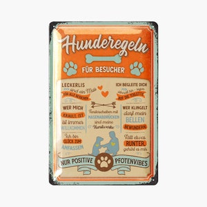 Op de afbeelding: Een rechthoekig metalen bord met een verweerde afwerking, met Duitse tekst en illustraties met honden als thema. Het bord heeft een oranje en blauwgroen kleurenschema met pootafdrukken en een botafbeelding. De tekst bevat zinnen als "hondenregels voor bezoekers".