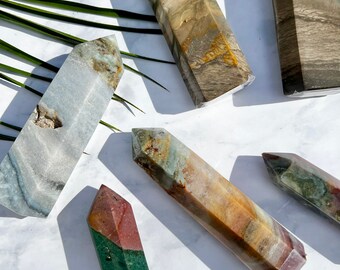 Puede incluir: Seis puntas de cristal de ágata pulidas de color verde, marrón y blanco. Las puntas están dispuestas sobre una superficie de mármol blanco.