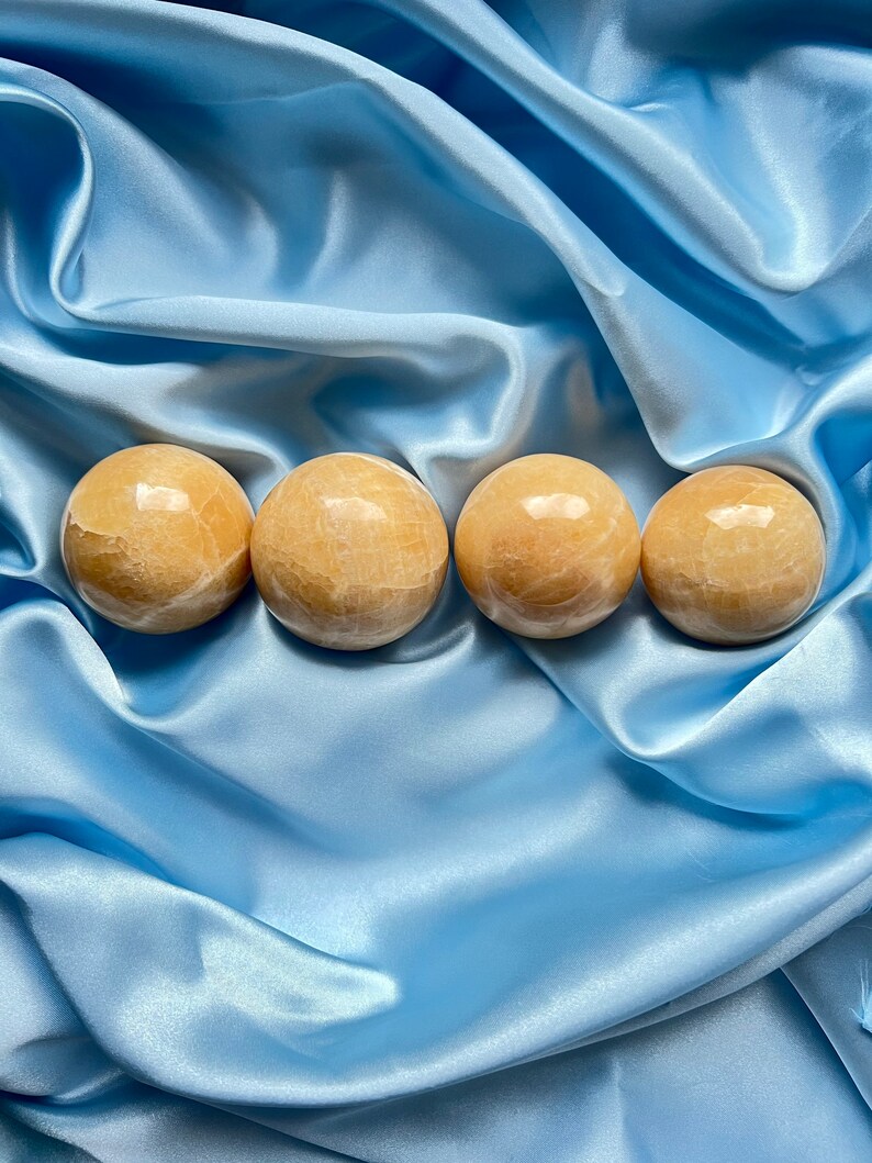 May include: Four smooth, round, light brown, polished, gemstone spheres on a blue satin fabric background.