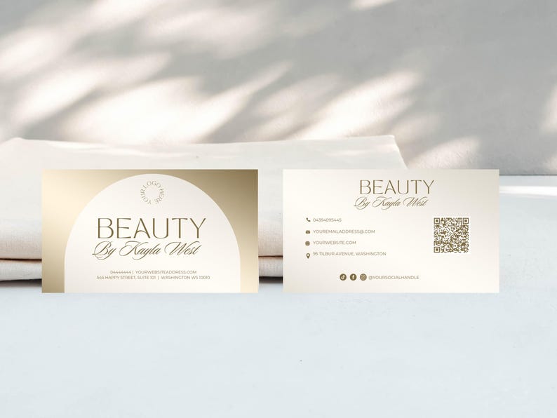 May include: A gold and white business card with the text "BEAUTY by Kayla West" and contact information. The card also includes a QR code.