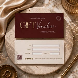 May include: A rectangular gift voucher set featuring a dark maroon card with gold text reading GIFT Voucher and a cream-coloured card with fields for To, From, Amount, and Expiry, including a QR code and social media icons at the bottom.