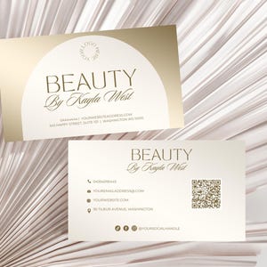May include: A white business card with gold text and a gold circle logo. The text reads "BEAUTY By Kayla West" and includes contact information such as a phone number, email address, website, and social media handle. The card also features a QR code.