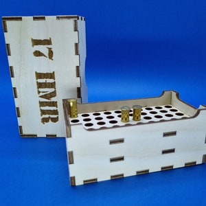 May include: A wooden box with a label that says "17 HMR" and a separate compartment with a grid of holes for storing small objects.