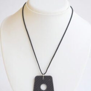 Può includere: Collana in pelle nera con un ciondolo quadrato e un ritaglio circolare. La collana è su un cordoncino nero.