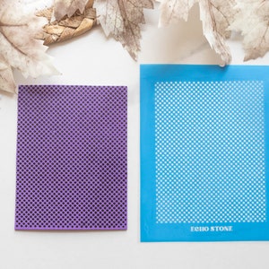 Può includere: Due stencil quadrati, uno viola e uno blu, con un motivo ripetitivo di piccoli cerchi. Lo stencil blu ha la scritta "ECHO STONE" stampata in basso.