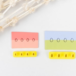 May include: Two rectangular cards with different colored backgrounds and rows of black circles. The cards are on a white surface. Below each card is a yellow plastic mold with five holes in the shape of circles.