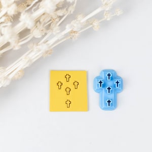 Puede incluir: Una tarjeta amarilla con un patrón de nueve cruces pequeñas y una cruz de plástico azul con un patrón de siete cruces pequeñas.