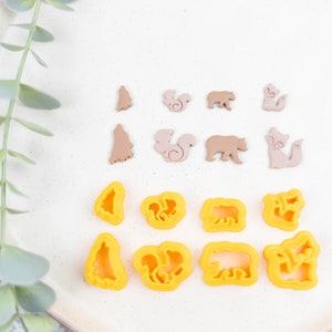 Puede incluir: Un plato blanco con una rama verde frondosa en el lado izquierdo. El plato tiene dos filas de cortadores de galletas marrones y amarillos en forma de árbol, ardilla, oso y zorro.