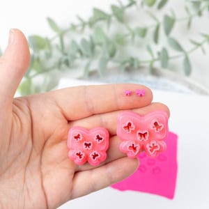 May include: Three pink plastic butterfly-shaped cookie cutters of different sizes. The largest cutter has five butterflies, the medium cutter has four butterflies, and the smallest cutter has two butterflies.