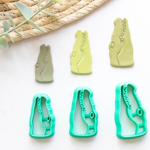 May include: Set of five green and light green alligator head cookie cutters. The cutters are in various sizes and are made of plastic.