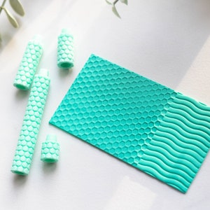 May include: Four turquoise blue textured rollers with a honeycomb pattern. The rollers are on a white surface next to a turquoise blue textured sheet with a honeycomb pattern on one side and a wavy pattern on the other side.