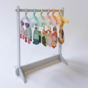 May include: A set of colourful polymer clay earrings displayed on a white hanger. The earrings feature various designs, including a flower, a lava lamp, and a geometric shape.