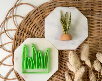 May include: Two white octagonal ceramic tiles with green and yellow clay plant shapes. The green shape is a grass cutter and the yellow shape is a potted snake plant.