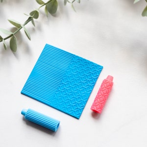 May include: Two blue textured rollers and a pink textured roller on a white surface. The rollers are used for crafting and creating patterns on clay or fondant.