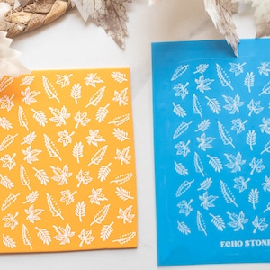 May include: Two rectangular sheets with leaf patterns. One is orange with white leaves, the other is blue with white leaves. The blue sheet has the text "ECHO STONE" at the bottom. The image has a fall theme.