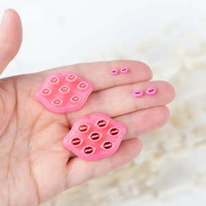 Peut inclure: Deux moules en silicone rose en forme de lèvres, chacun avec neuf formes de lèvres individuelles. Trois plus petits moules en silicone rose en forme de lèvres sont également représentés.