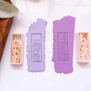 Peut inclure: Trois tampons rectangulaires en argile polymère avec un motif floral. Les tampons sont dans différentes nuances de violet et de rose.