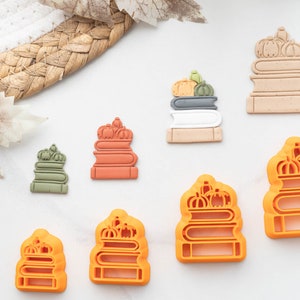 Peut inclure: Ensemble de neuf emporte-pièces en forme de piles de livres surmontées de citrouilles. Les emporte-pièces sont de différentes couleurs, notamment orange, vert, marron et gris.