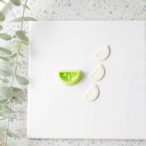 May include: A set of four green and white plastic cookie cutters shaped like watermelon slices. The cutters are on a white surface.
